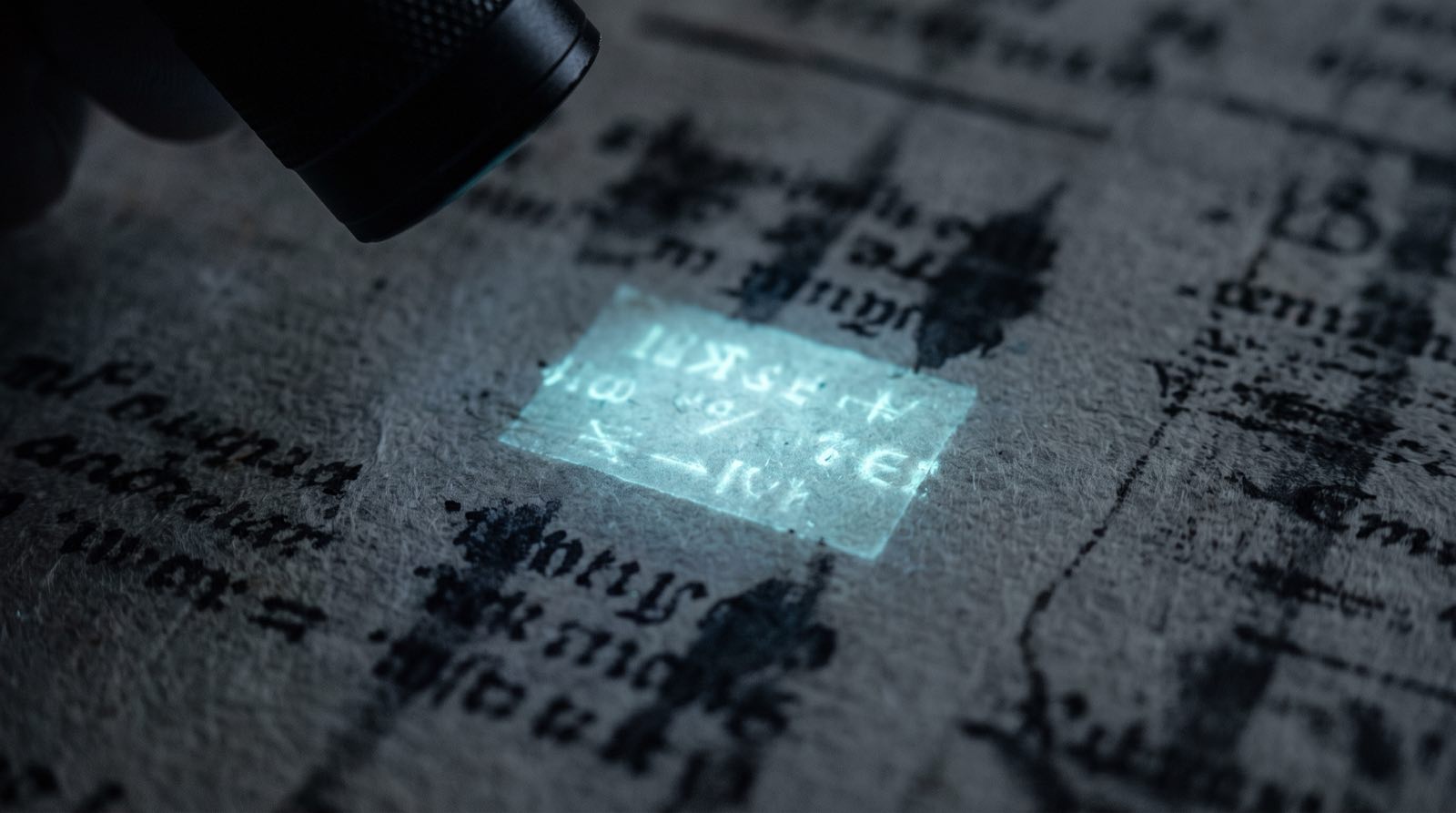 Macro fotografia di un foglio coperto di testo stampato, quasi tutto sfocato e illeggibile, tranne una piccola sezione che brilla di una luce ciano come rivelata da una luce speciale